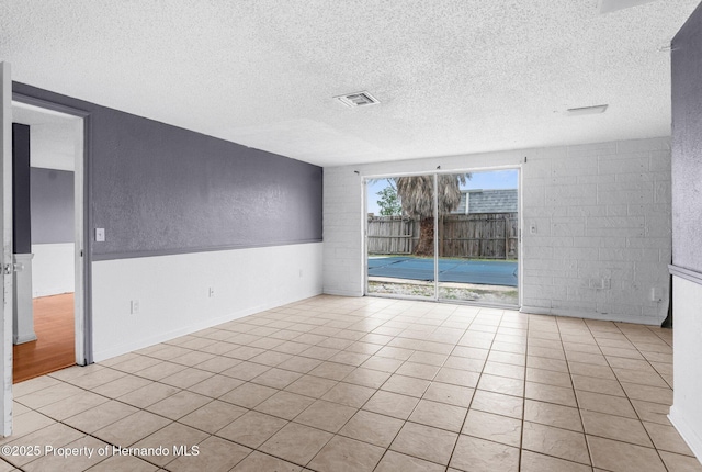 tiled empty room featuring visible vents, a textured ceiling, and a textured wall