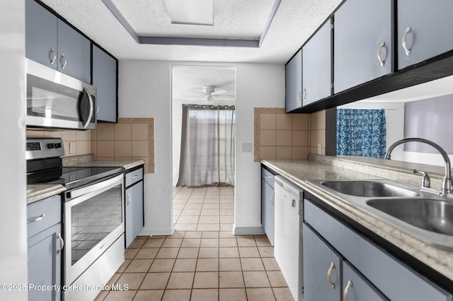 kitchen with a sink, a textured ceiling, tasteful backsplash, appliances with stainless steel finishes, and a raised ceiling