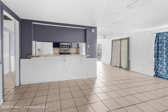 kitchen featuring a ceiling fan, tile countertops, a peninsula, appliances with stainless steel finishes, and a breakfast bar area