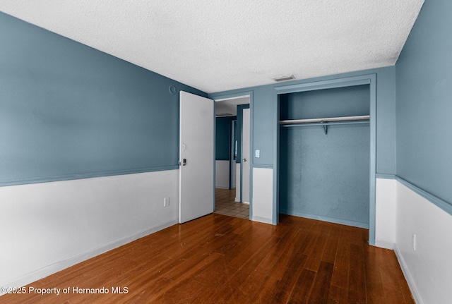 unfurnished bedroom featuring wood finished floors, visible vents, baseboards, a closet, and a textured ceiling