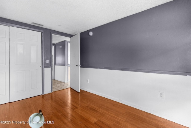 unfurnished bedroom with visible vents, a textured ceiling, baseboards, and wood finished floors