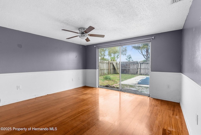 unfurnished room with a wainscoted wall, a textured ceiling, ceiling fan, and wood finished floors