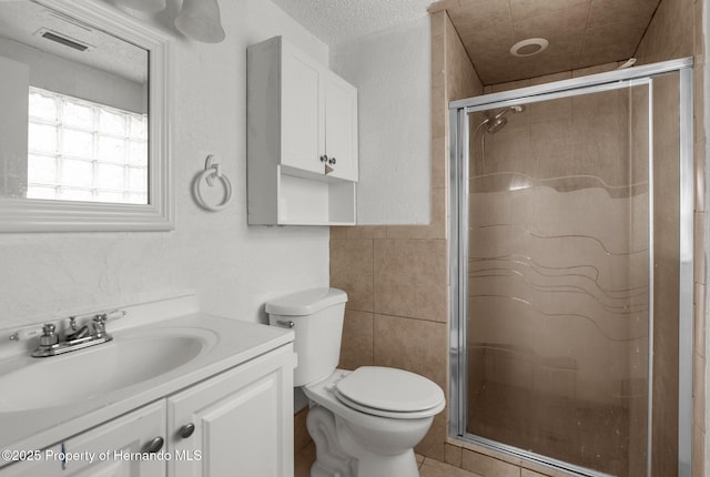 full bath with vanity, visible vents, a stall shower, a textured ceiling, and tile walls