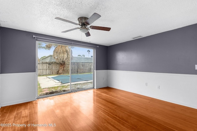 empty room with visible vents, a wainscoted wall, a textured ceiling, and wood finished floors