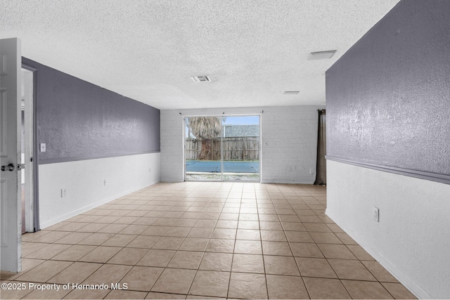 spare room with light tile patterned floors, a textured ceiling, and a textured wall