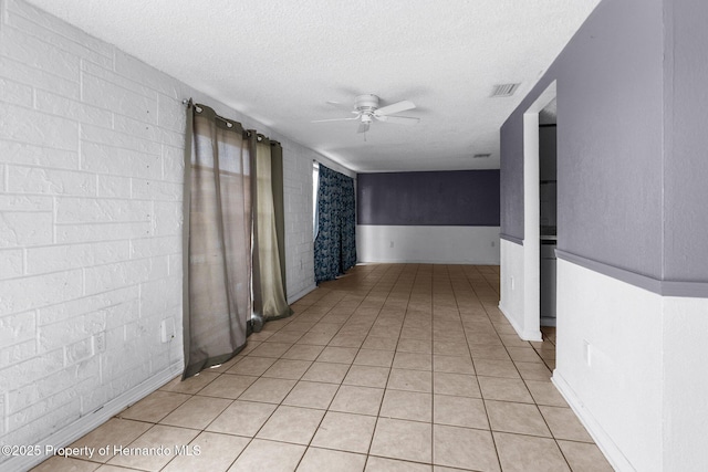 hallway with light tile patterned flooring, visible vents, wainscoting, and a textured ceiling