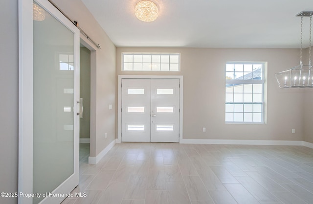 foyer entrance featuring a chandelier, a barn door, and baseboards