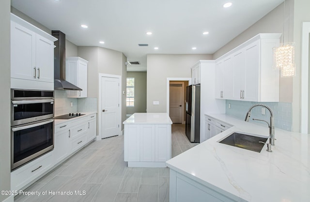 kitchen with stainless steel appliances, white cabinetry, a kitchen island, a sink, and wall chimney exhaust hood