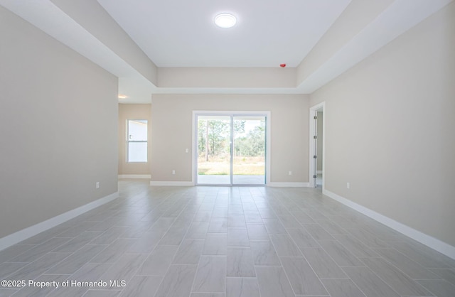 spare room featuring a tray ceiling and baseboards