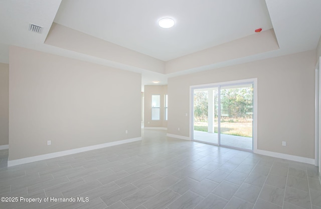 spare room featuring a raised ceiling, visible vents, and baseboards