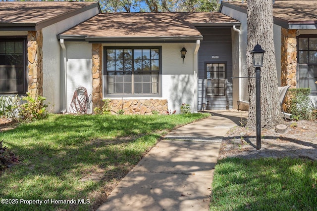 entrance to property with stone siding, a lawn, roof with shingles, and stucco siding