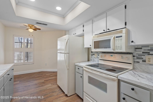 kitchen featuring white appliances, visible vents, a raised ceiling, wood finished floors, and backsplash