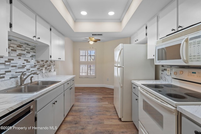 kitchen with dark wood-style floors, a tray ceiling, visible vents, a sink, and white appliances