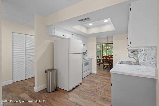 kitchen featuring a tray ceiling, light countertops, visible vents, a sink, and white appliances