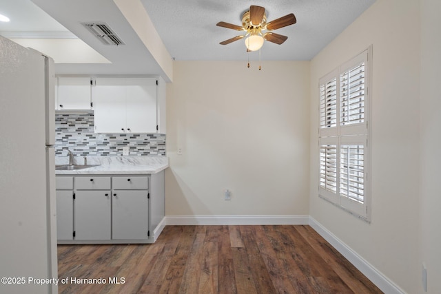 kitchen with a sink, visible vents, baseboards, tasteful backsplash, and dark wood finished floors