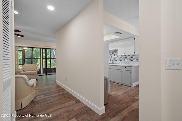 hallway with recessed lighting, visible vents, dark wood-type flooring, a sink, and baseboards