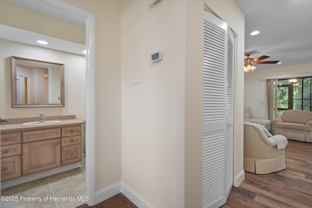 corridor featuring light wood-type flooring, recessed lighting, a sink, and baseboards