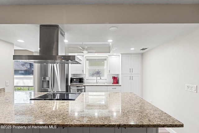 kitchen with island range hood, light stone countertops, stainless steel appliances, white cabinetry, and a sink