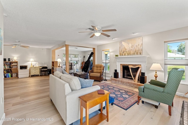 living area featuring a textured ceiling, ceiling fan, a fireplace, and light wood-style floors