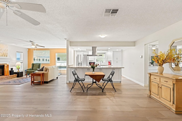 dining space featuring a fireplace, visible vents, a textured ceiling, light wood-type flooring, and baseboards