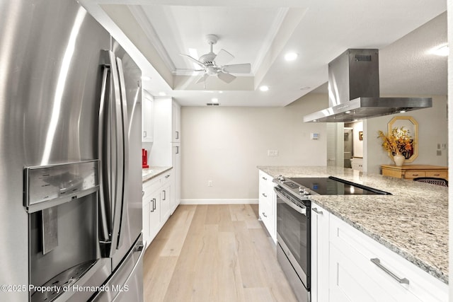 kitchen with island exhaust hood, stainless steel appliances, white cabinetry, light wood finished floors, and a raised ceiling