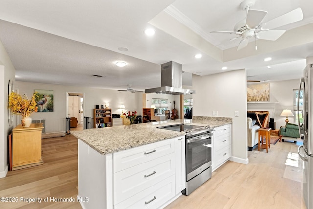 kitchen with a peninsula, a fireplace, light wood finished floors, island exhaust hood, and stainless steel range with electric stovetop