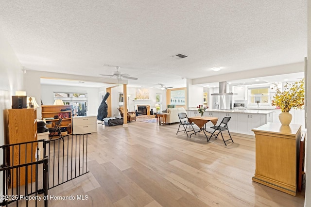 interior space featuring visible vents, light wood-type flooring, a glass covered fireplace, and a wealth of natural light