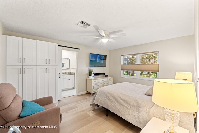 bedroom with visible vents, ensuite bathroom, a textured ceiling, light wood-style floors, and a sink