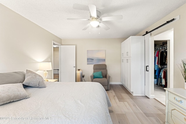 bedroom featuring light wood finished floors, a barn door, ceiling fan, a walk in closet, and a textured ceiling