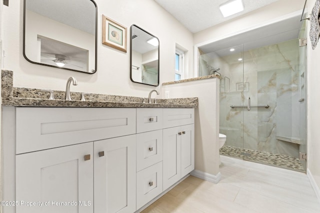 full bathroom featuring double vanity, baseboards, toilet, a shower stall, and a sink