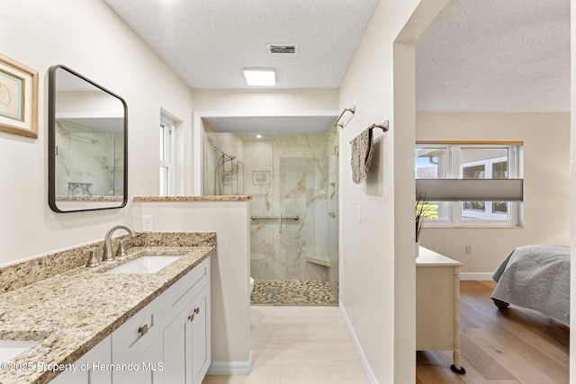 full bath featuring visible vents, a stall shower, vanity, a textured ceiling, and baseboards