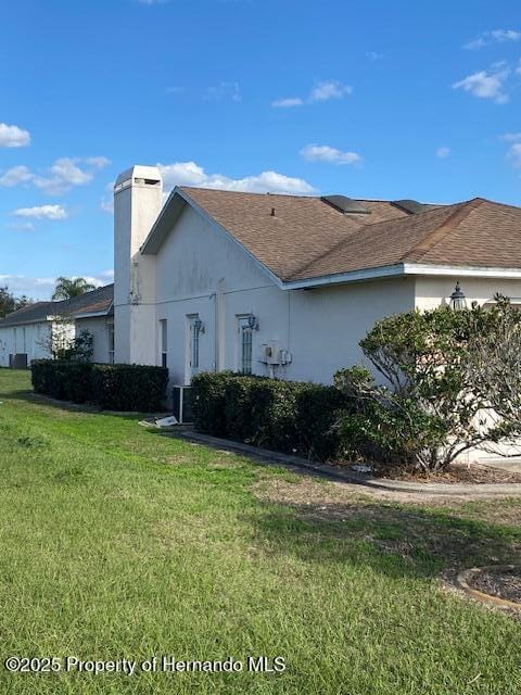 view of front of property with roof with shingles, a front lawn, a chimney, and stucco siding