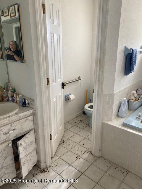 full bathroom featuring a relaxing tiled tub, vanity, and toilet