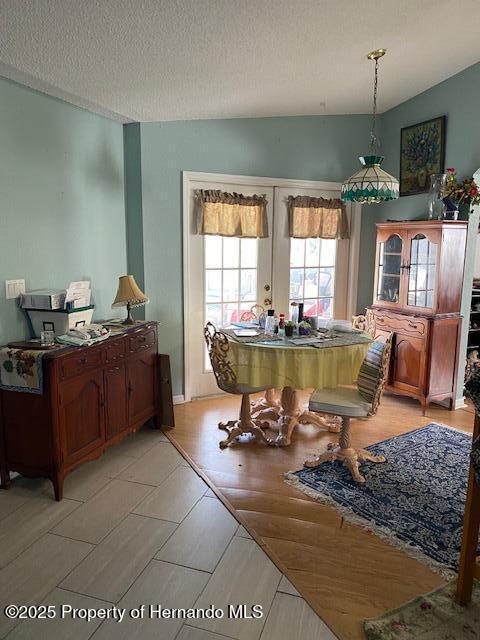 dining room with a textured ceiling, french doors, and light wood-style flooring