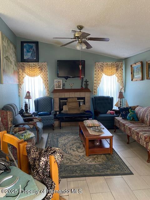 living room with ceiling fan, vaulted ceiling, a wealth of natural light, and a tile fireplace