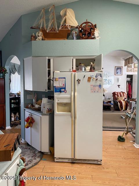 kitchen featuring arched walkways, white refrigerator with ice dispenser, light wood-type flooring, and lofted ceiling