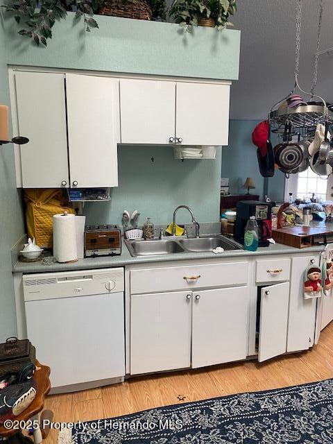 kitchen featuring light countertops, white cabinets, white dishwasher, and a sink