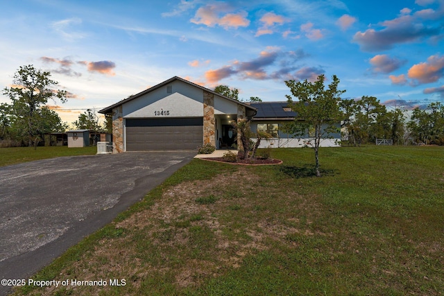 13415 Ester Dr, Brooksville, FL 34613 - view of front of house featuring a lawn, driveway, stone siding, roof mounted solar panels, and a garage