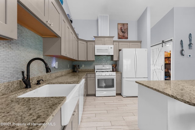 13415 Ester Dr, Brooksville, FL 34613 - kitchen with a barn door, light stone counters, backsplash, white appliances, and light wood-type flooring