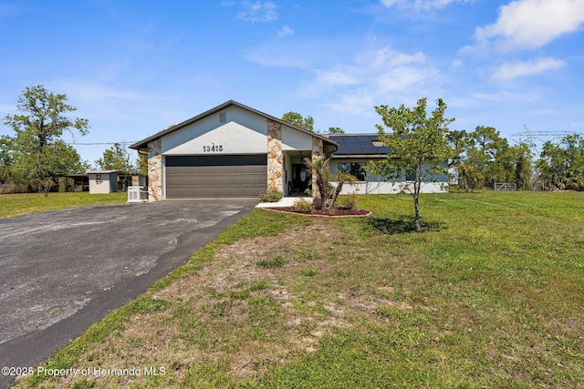 13415 Ester Dr, Brooksville, FL 34613 - view of front facade featuring a front lawn, driveway, stone siding, an attached garage, and roof mounted solar panels