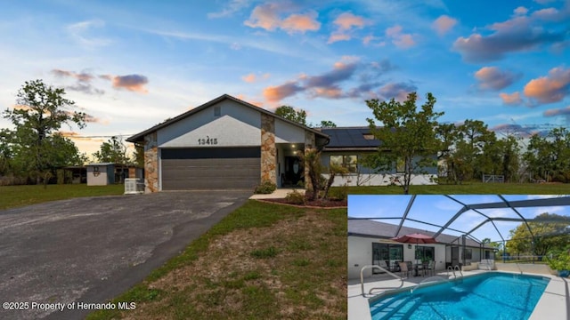 13415 Ester Dr, Brooksville, FL 34613 - view of front of house with a garage, roof mounted solar panels, stone siding, and aphalt driveway