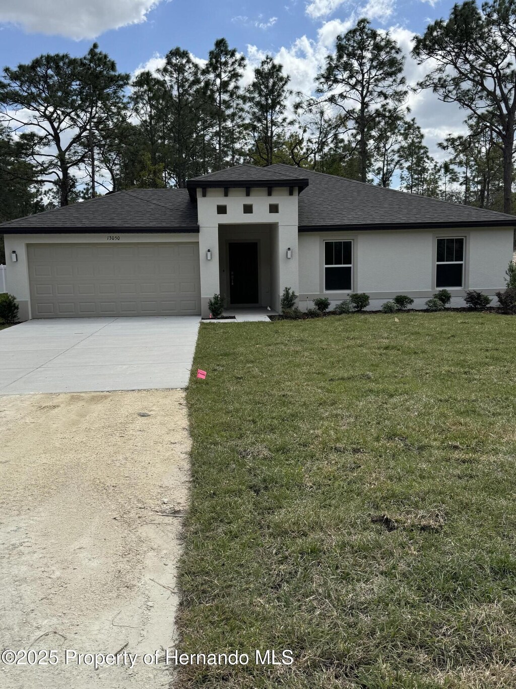 prairie-style home with concrete driveway, stucco siding, an attached garage, a front lawn, and a shingled roof