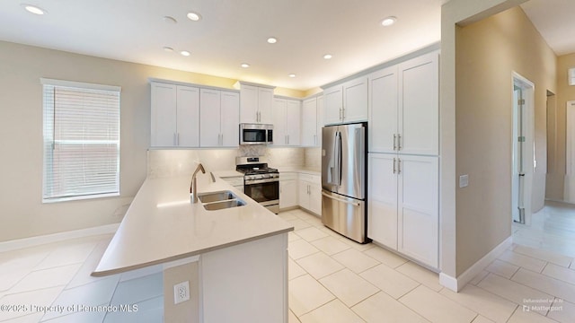 kitchen featuring stainless steel appliances, light countertops, decorative backsplash, a sink, and a peninsula