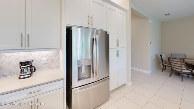 kitchen with light tile patterned floors, light countertops, backsplash, white cabinetry, and stainless steel fridge