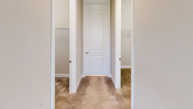 hall with a textured wall, carpet, and baseboards