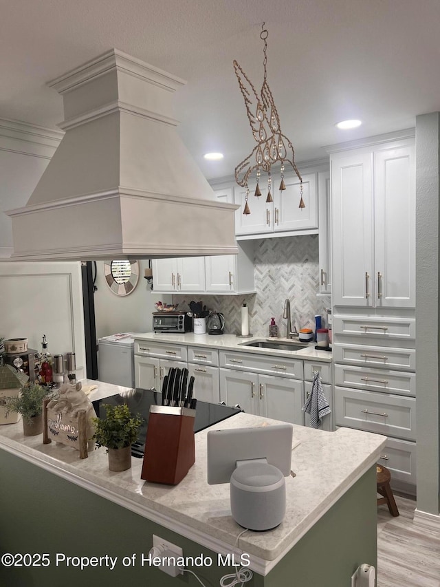 kitchen with light wood finished floors, tasteful backsplash, white cabinets, a sink, and premium range hood