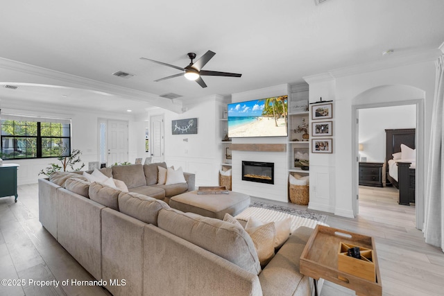 living area featuring visible vents, ornamental molding, light wood-style floors, a fireplace, and a decorative wall