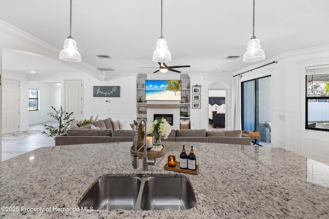 kitchen featuring a wainscoted wall, a glass covered fireplace, crown molding, a decorative wall, and light stone countertops