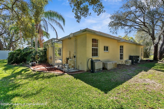 rear view of property featuring a yard, fence, and stucco siding