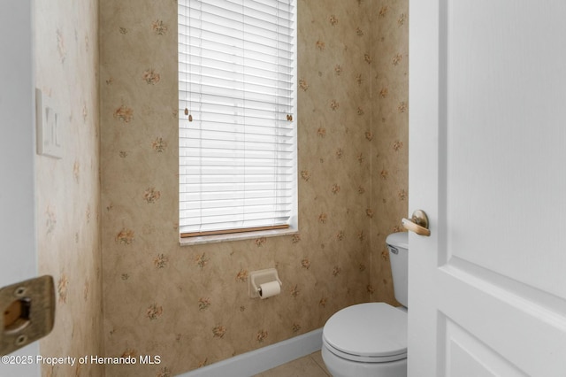 bathroom featuring toilet, wallpapered walls, and baseboards